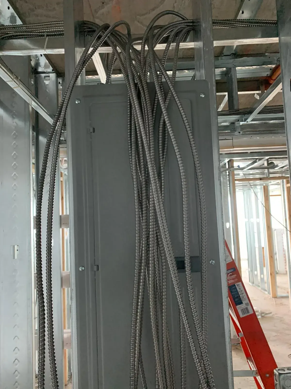 Gray panel in metal stud framing with a bundle of flexible metal-clad cables hanging in front of it