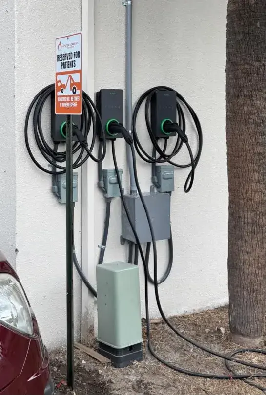 Three wall-mounted EV chargers with coiled cables, each above a gray disconnect switch