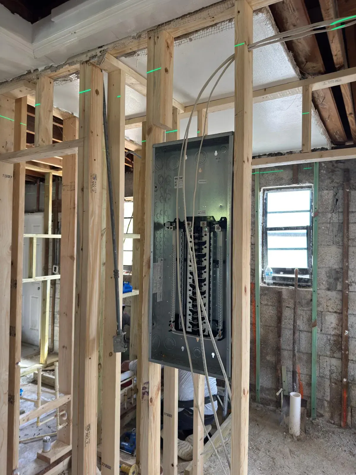Empty breaker panel enclosure mounted between new wood studs with white cables hanging in front
